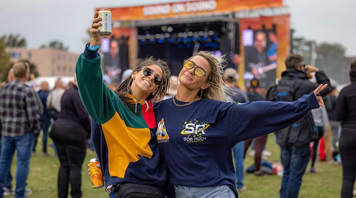 Two young women under stage holding beers facing camera